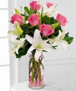 Fragrant white lilies & elegant pink roses are wrapped up with pink wire in a clear glass vase with pink gems.